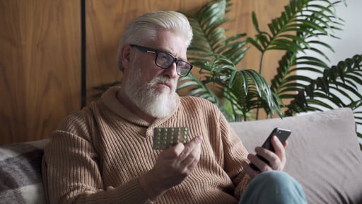 An-elderly-man-is-sitting-alone-on-the-couch-a-patient-is-wearing-glasses-reading-instructions-on-a-smartphone-how-to-take-pills-1284584548_3840x2160-3